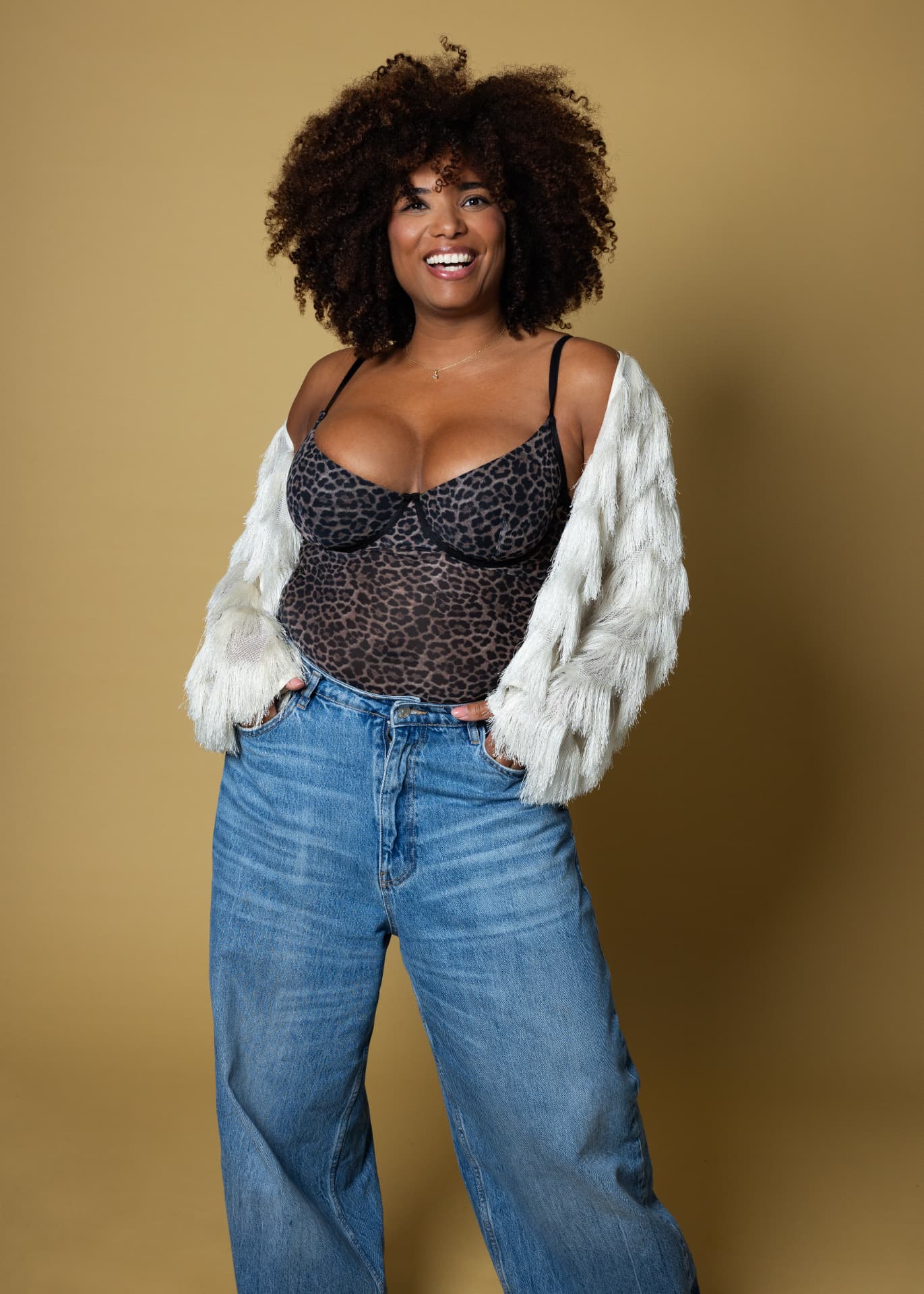 Robin-April staand in jeans en luipaardtop, oker achtergrond